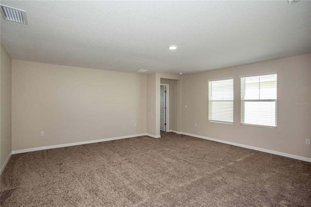 An empty room with beige walls, brown carpet, and two windows with white blinds — 9062 BELLEVIEW FOREST PASS, DADE CITY, FL