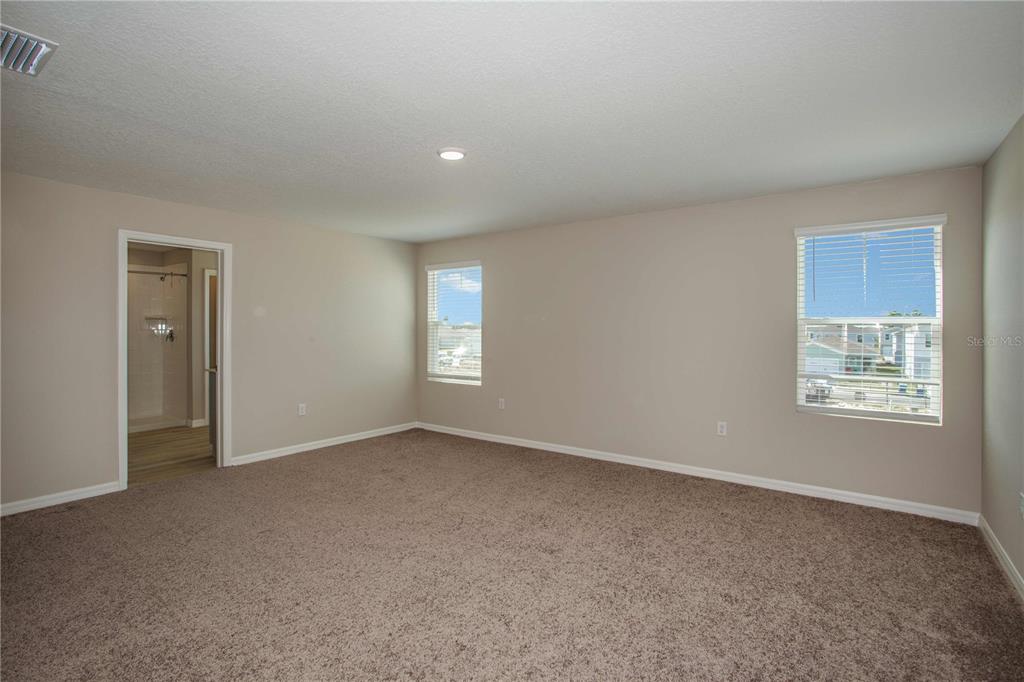 A carpeted bedroom features beige walls, two windows, and a doorway leading to a bathroom — 9062 BELLEVIEW FOREST PASS, DADE CITY, FL