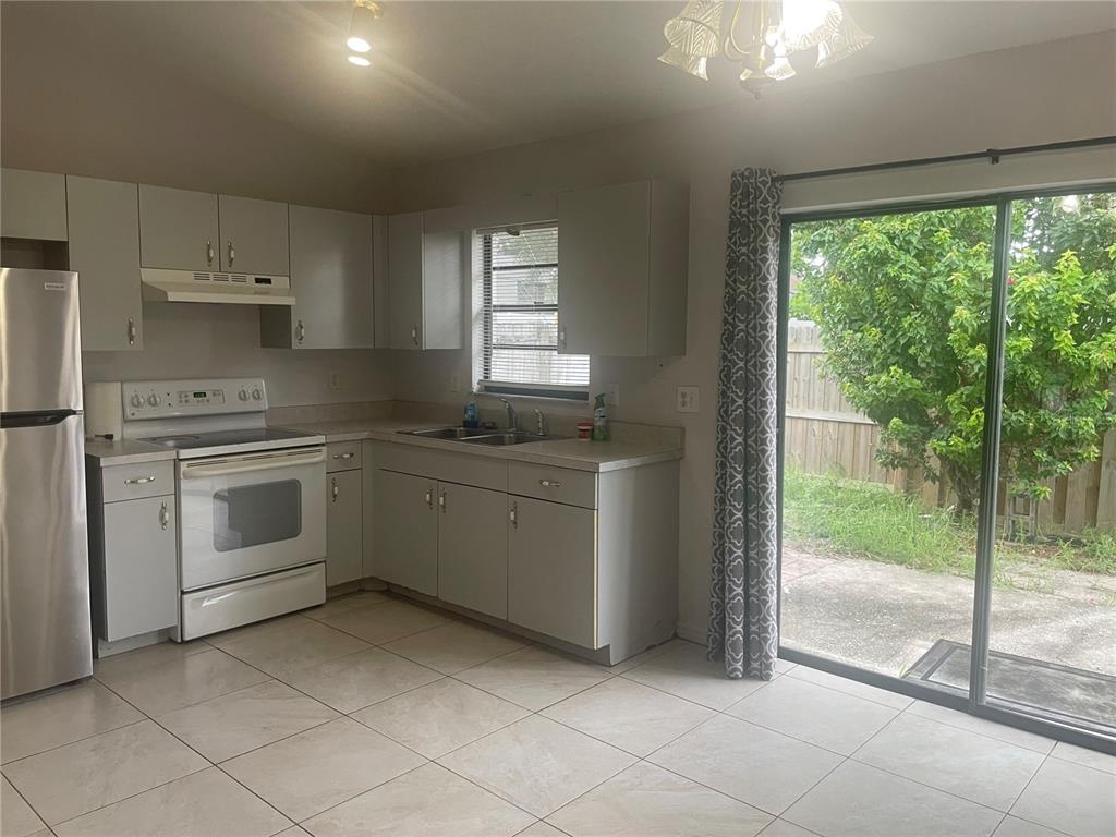 A kitchen with grey cabinets, white appliances, tile flooring, and a sliding glass patio door — 1349 PIERCE STREET, CLEARWATER, FL