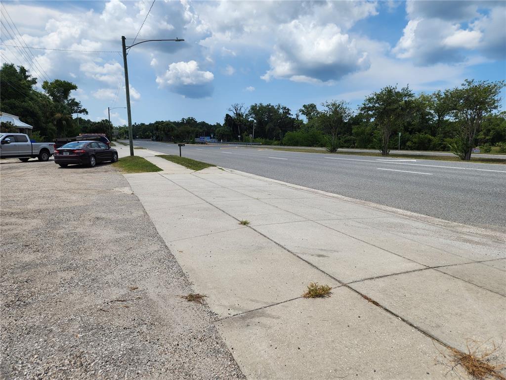 A sidewalk runs alongside a paved road with parked cars on the left — 123 HWY 19, INGLIS, FL