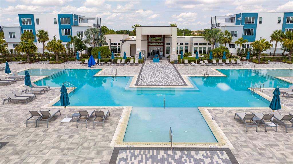 An outdoor swimming pool with lounge chairs and umbrellas sits between two modern apartment buildings — 7770 SANDY RIDGE DRIVE UNIT 219, REUNION, FL