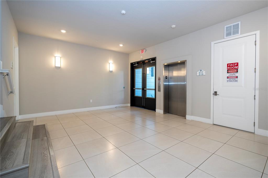 A tiled lobby features an elevator, a double glass door, and a utility room door — 7770 SANDY RIDGE DRIVE UNIT 219, REUNION, FL