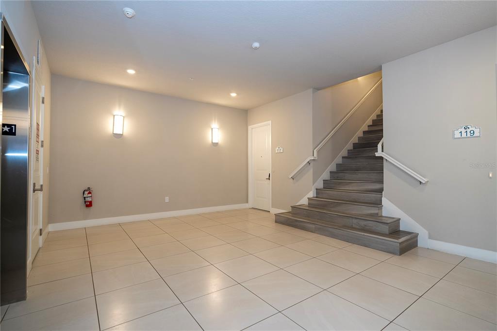 A tiled building lobby features an elevator, a staircase, and a door labeled 117 — 7770 SANDY RIDGE DRIVE UNIT 219, REUNION, FL