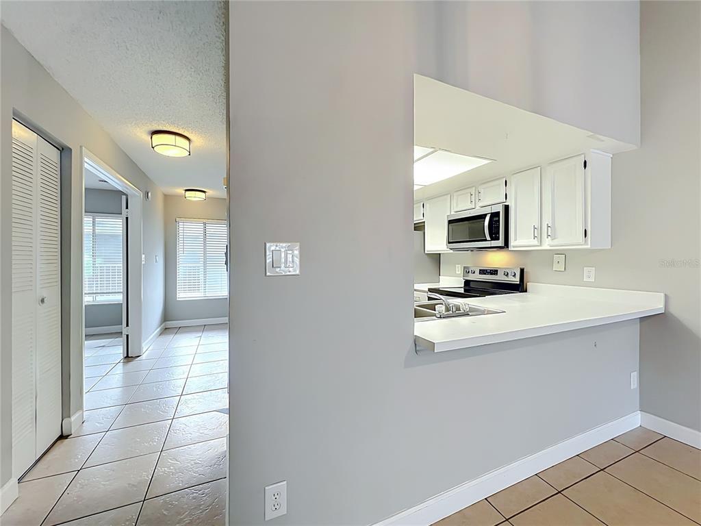 A tiled kitchen with stainless steel appliances sits adjacent to a hallway and laundry closet — 4370 WHITE PINE AVENUE UNIT 2, ORLANDO, FL