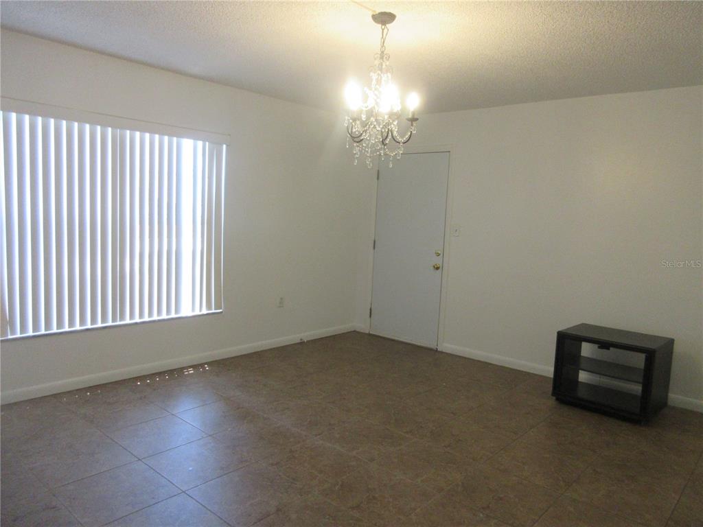 A room with white walls, tile flooring, a crystal chandelier, and a window with blinds — 2410 SE 16TH AVENUE UNIT H, OCALA, FL