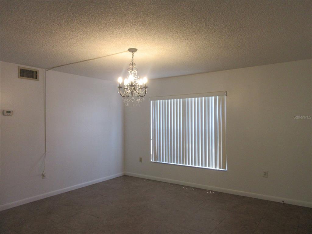 A dining room features a crystal chandelier, vertical blinds on a window, and tile flooring — 2410 SE 16TH AVENUE UNIT H, OCALA, FL
