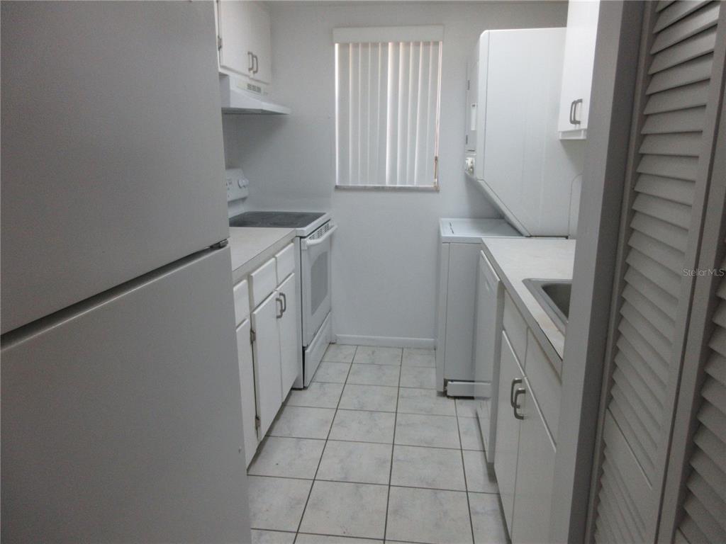 A narrow galley kitchen features white cabinets, white appliances, and light-colored tile flooring — 2410 SE 16TH AVENUE UNIT H, OCALA, FL