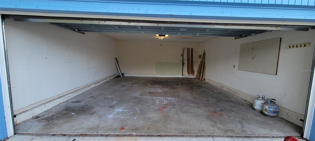 An empty two-car garage with a concrete floor, white walls, and a pegboard storage panel — 1425 NE OLD MILL DRIVE, DELTONA, FL