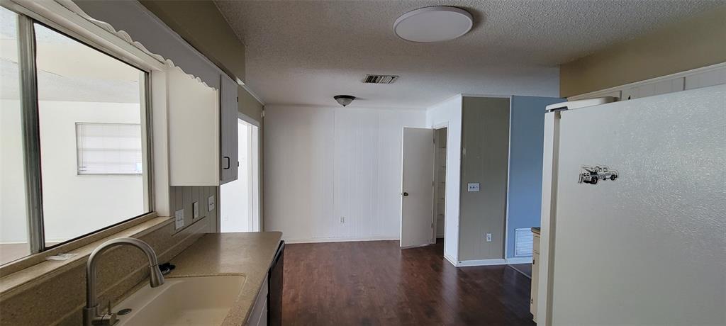 A kitchen with a sink, white cabinets, and dark wood flooring looking toward a doorway — 1425 NE OLD MILL DRIVE, DELTONA, FL