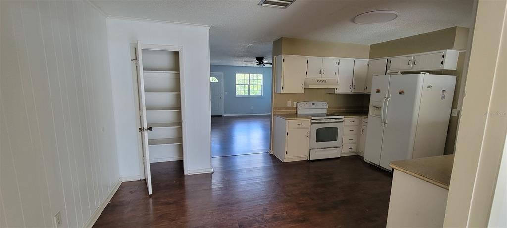 A kitchen with white cabinets, a white refrigerator, and a pantry opens to a living area — 1425 NE OLD MILL DRIVE, DELTONA, FL