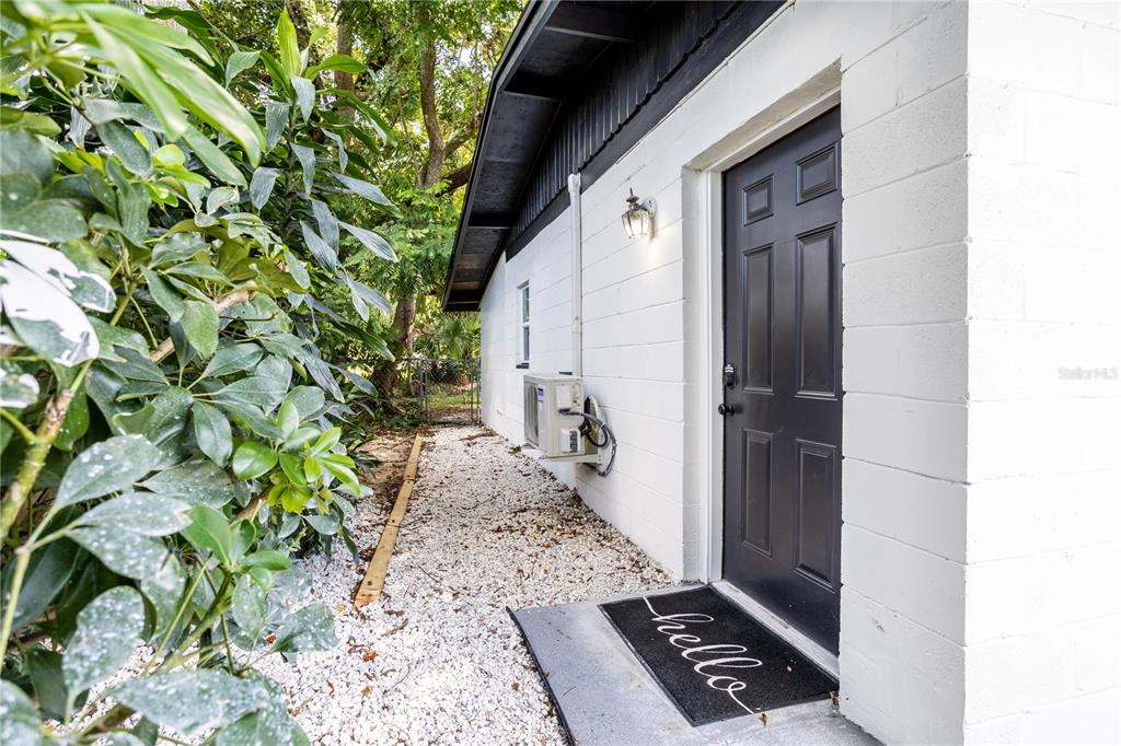 A side view of a white concrete block house with a dark door and gravel path — 1213 CORBETT LANE UNIT 2, ORLANDO, FL