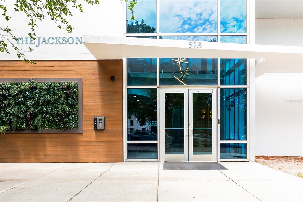 The exterior entrance of a modern building features a glass door, wood paneling, and greenery — 525 E JACKSON STREET UNIT 507, ORLANDO, FL