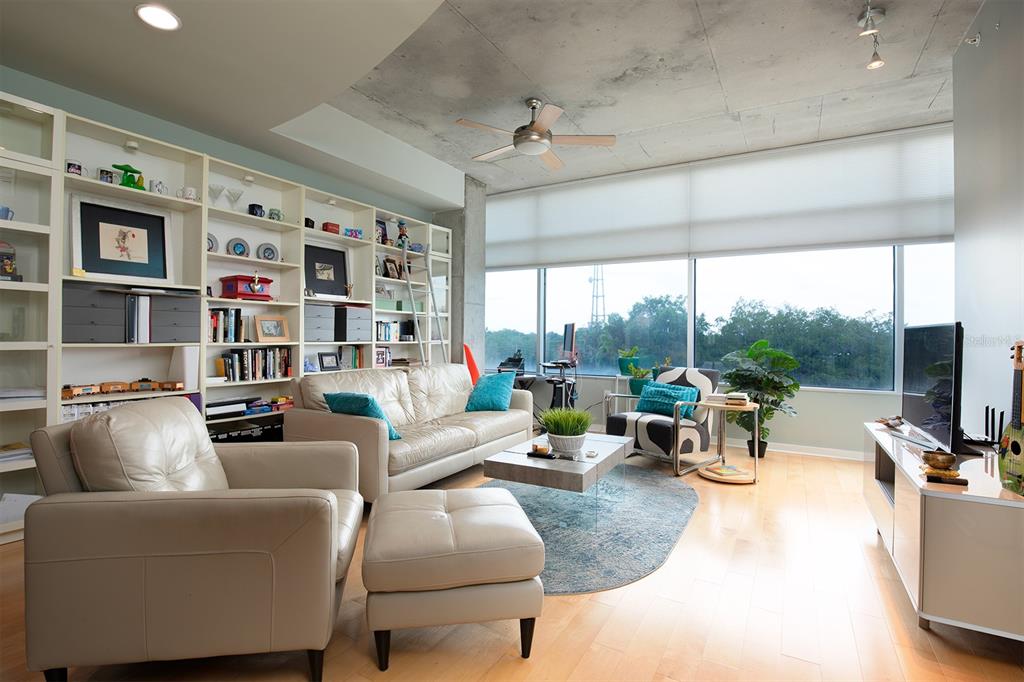A living room features a concrete ceiling, built-in shelving, leather furniture, and large windows — 525 E JACKSON STREET UNIT 507, ORLANDO, FL