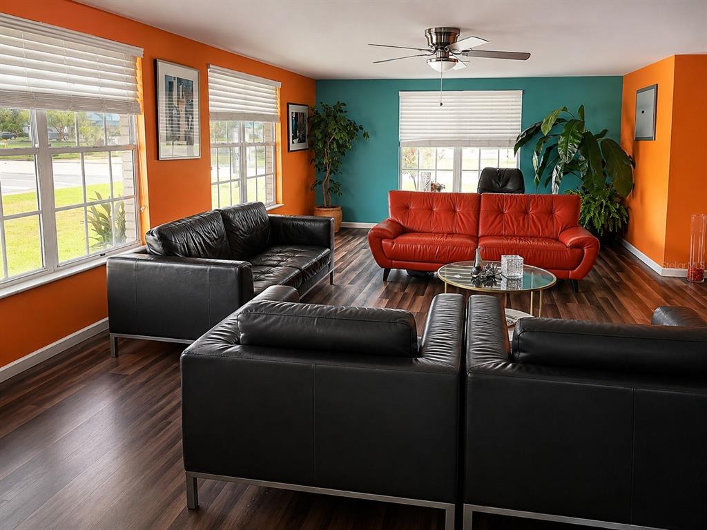 A living room features orange and teal walls, black and red leather sofas, and wood flooring — 399 AVENUE K SE, WINTER HAVEN, FL