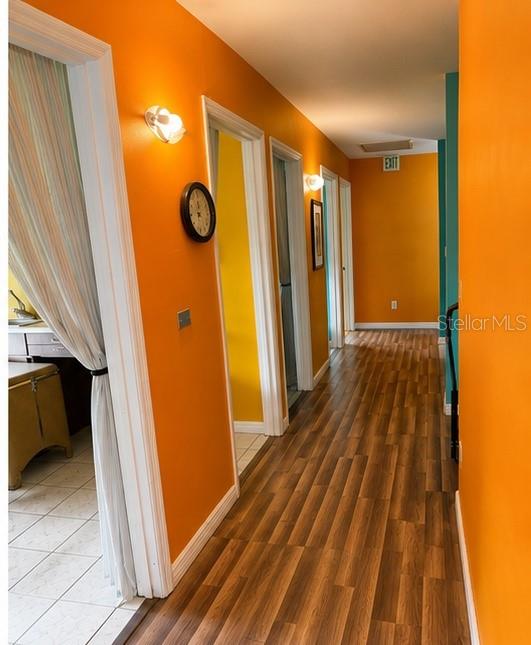 A hallway with orange walls, wood-look flooring, and multiple doorways leads to an exit sign — 399 AVENUE K SE, WINTER HAVEN, FL