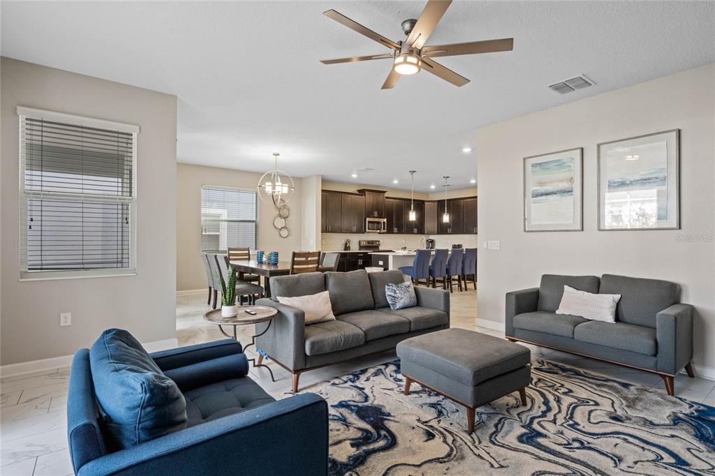 An open-concept living room features gray sofas, a blue armchair, and an adjacent dining area — 1565 MULLIGAN BOULEVARD, DAVENPORT, FL