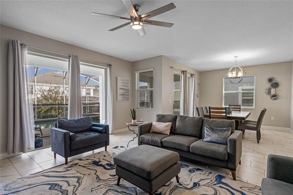 A living room with a gray sofa, matching armchair, ottoman, and dining area with tile floors — 1565 MULLIGAN BOULEVARD, DAVENPORT, FL