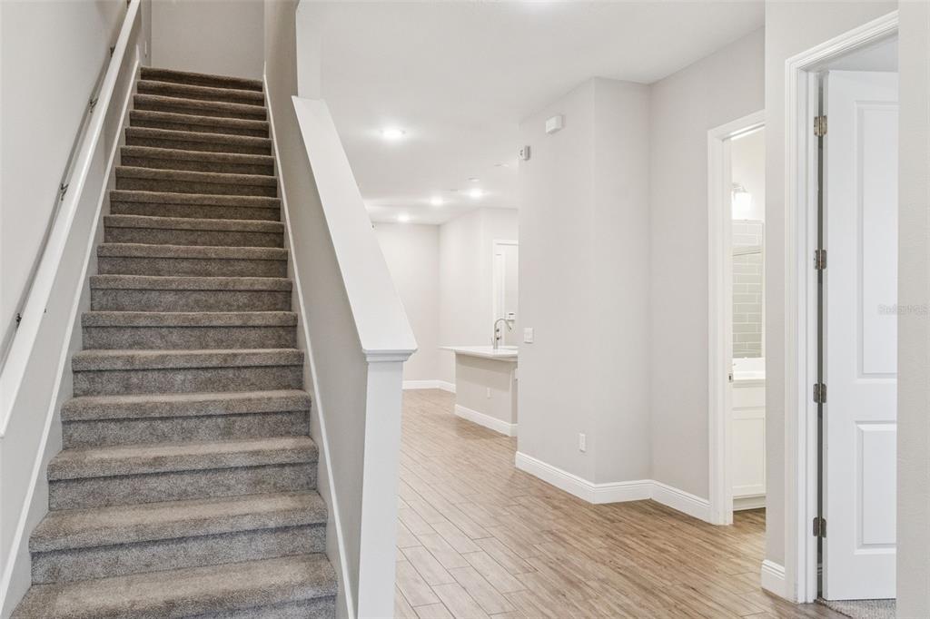 A carpeted staircase leads upward next to a hallway with wood-look tile flooring — 6447 CYRILS DRIVE, ST CLOUD, FL