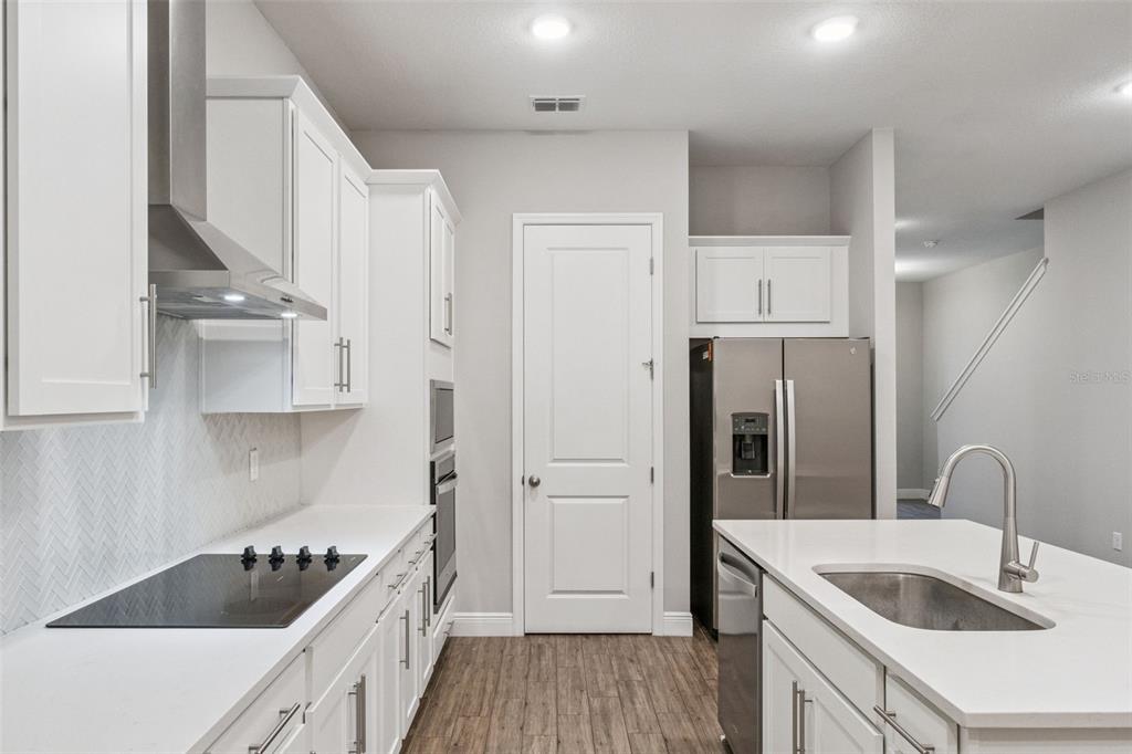 A modern kitchen features white cabinetry, stainless steel appliances, a center island, and wood flooring — 6447 CYRILS DRIVE, ST CLOUD, FL