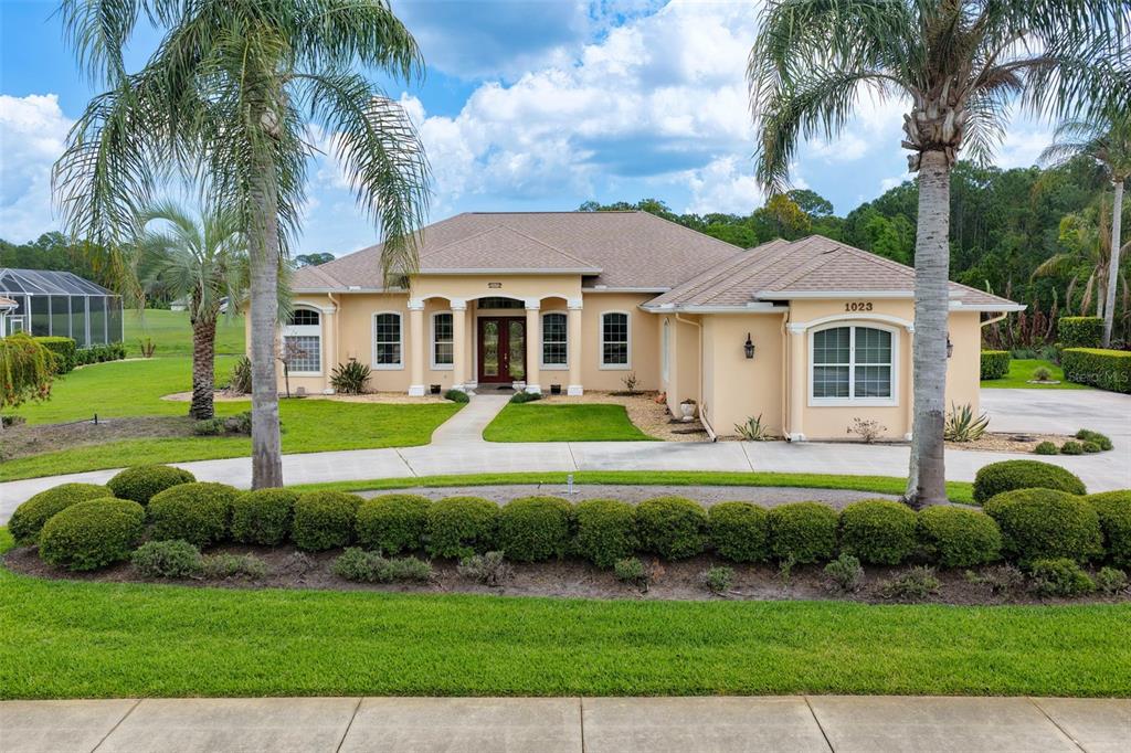 A single-story tan house with a tiled roof, arched entryway, and palm trees in front — 1023 HAMPSTEAD LANE, ORMOND BEACH, FL