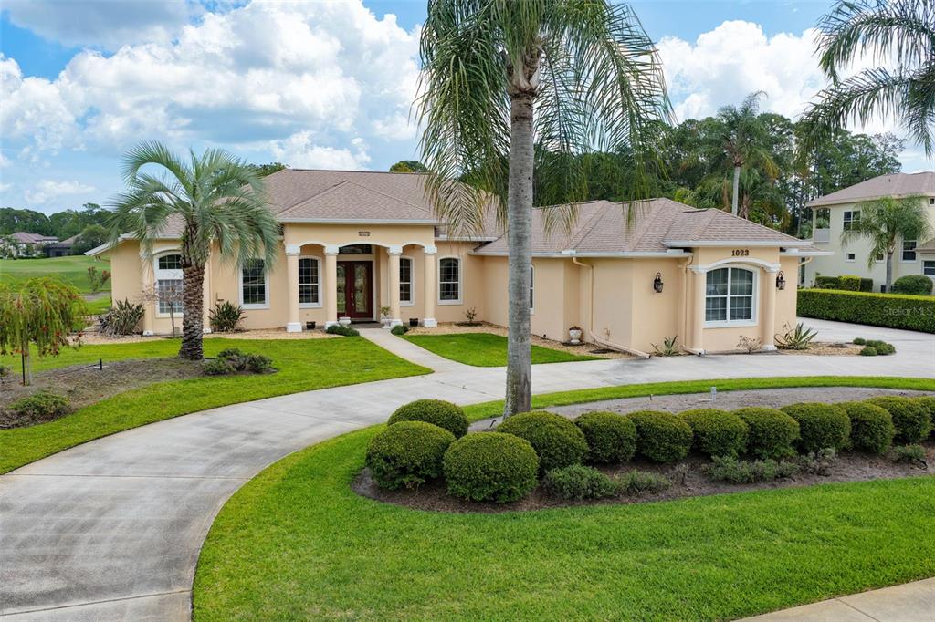 A tan single-story house with a curved driveway, palm trees, and manicured landscaping — 1023 HAMPSTEAD LANE, ORMOND BEACH, FL