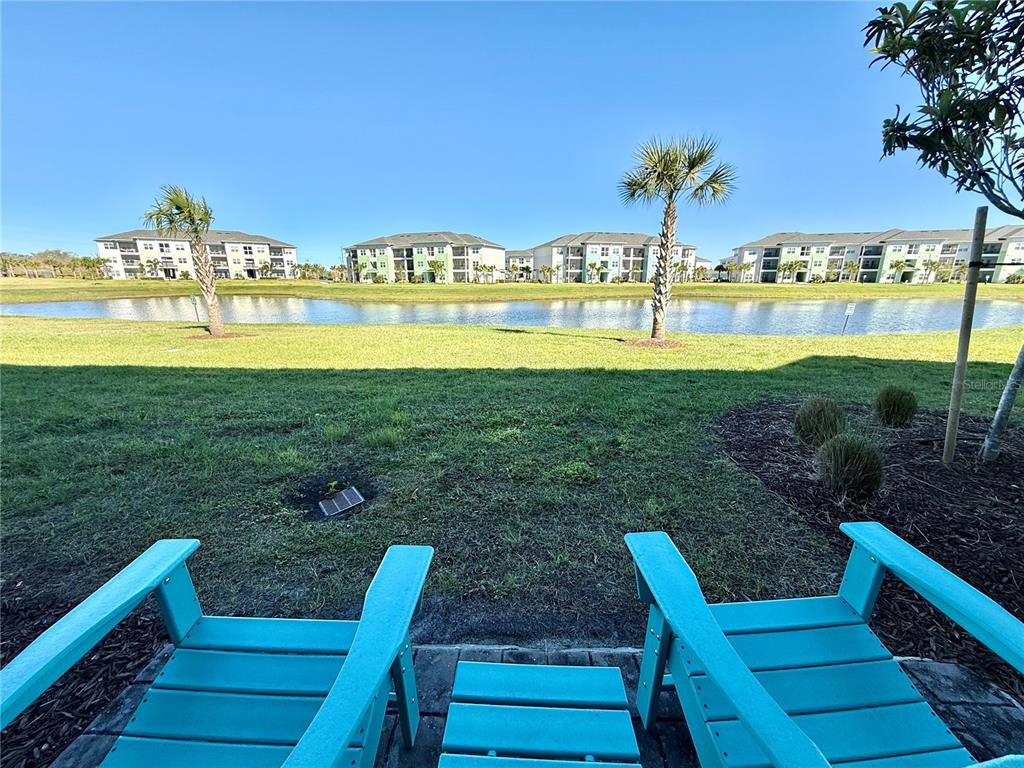 Two turquoise Adirondack chairs sit on a patio overlooking a pond and apartment buildings — 3117 CARIBBEAN SOUL DRIVE, KISSIMMEE, FL