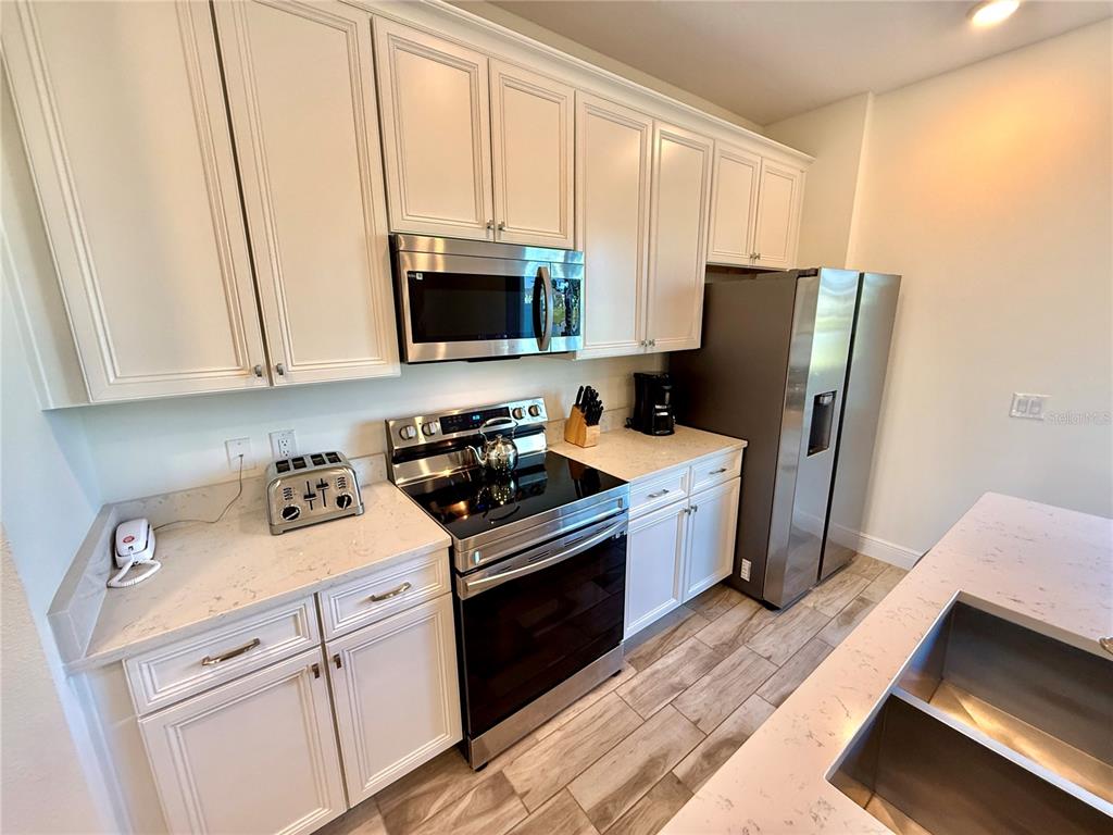A kitchen features white cabinets, stainless steel appliances, quartz countertops, and wood-look tile flooring — 3117 CARIBBEAN SOUL DRIVE, KISSIMMEE, FL