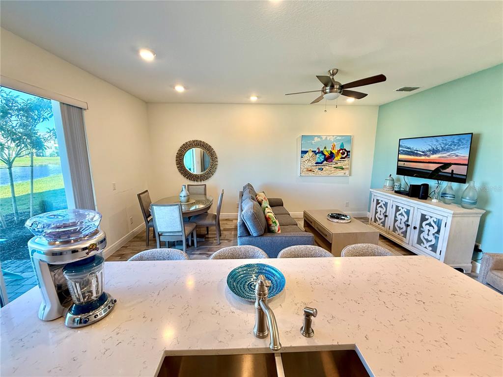 A kitchen island overlooks an open-concept living and dining area with light-colored furniture and decor — 3117 CARIBBEAN SOUL DRIVE, KISSIMMEE, FL