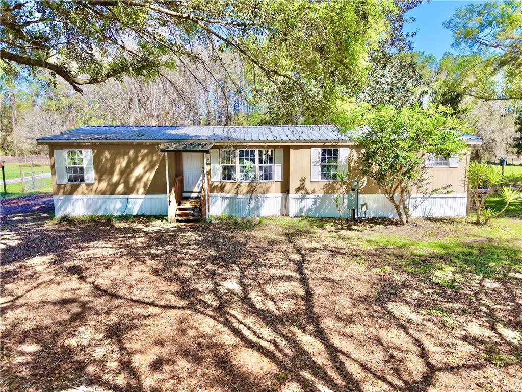 A single-story manufactured home with a metal roof sits on a wooded, grassy lot — 7494 GORDON LOOP, BROOKSVILLE, FL