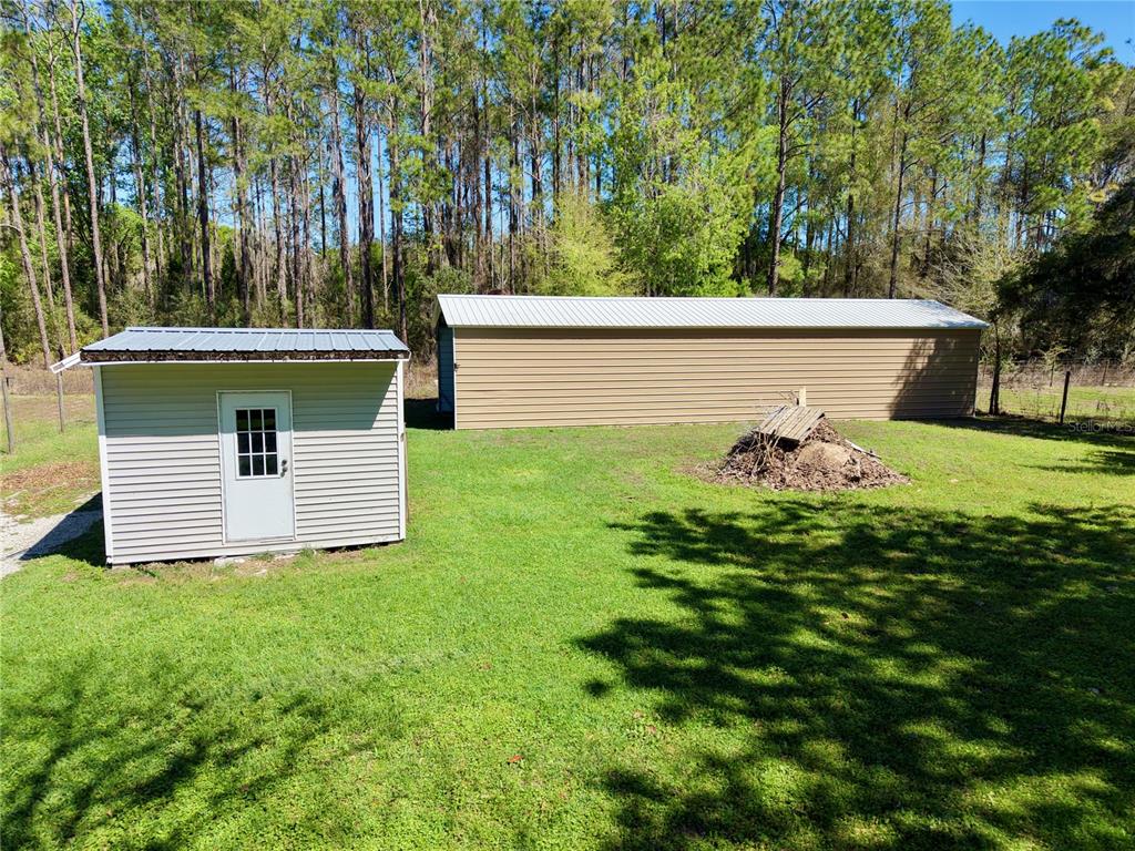 A small shed and a long metal storage building sit on a grassy backyard lot — 7494 GORDON LOOP, BROOKSVILLE, FL