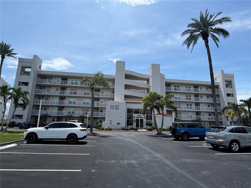 A multi-story apartment building with a parking lot and palm trees under a blue sky — 5701 BAHIA DEL MAR CIRCLE UNIT 407, ST PETERSBURG, FL