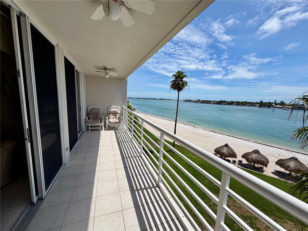 A balcony with white tile flooring overlooks a sandy beach, grassy lawn, and the ocean — 5701 BAHIA DEL MAR CIRCLE UNIT 407, ST PETERSBURG, FL
