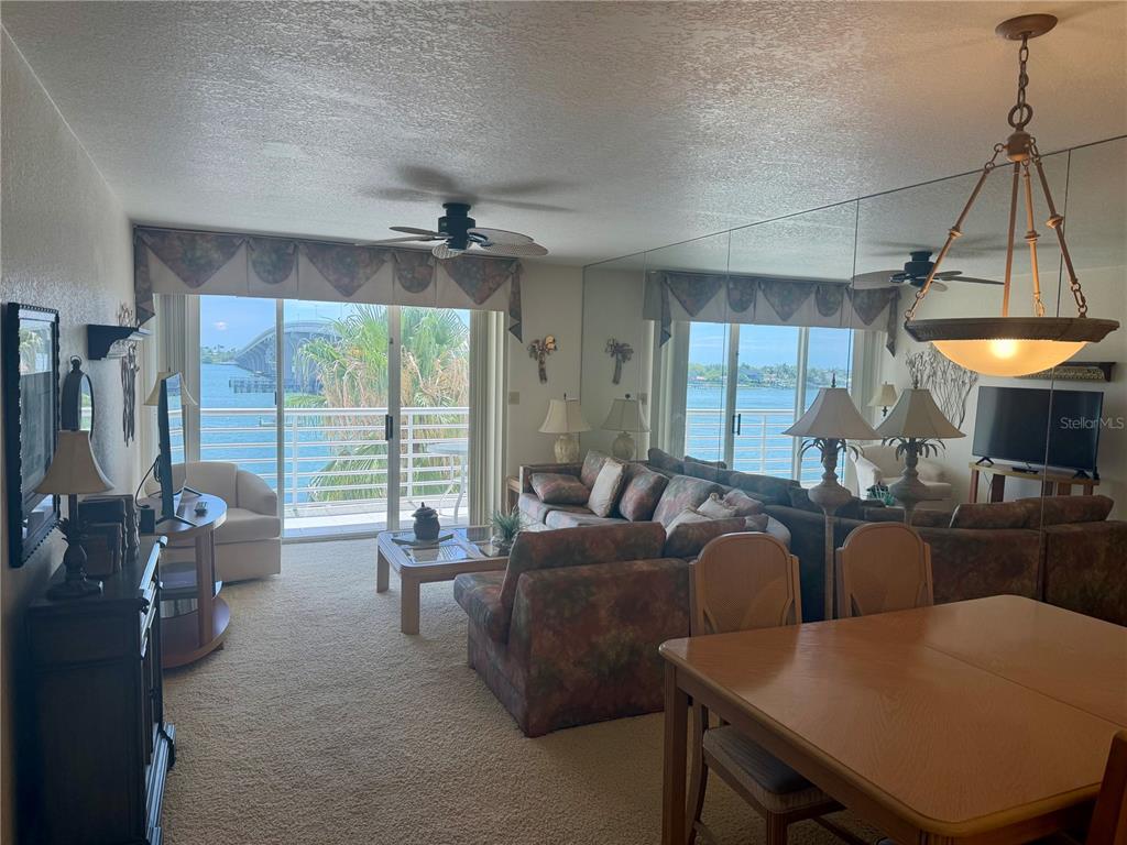 A living and dining area features mirrored walls, a ceiling fan, and a waterfront balcony view — 5701 BAHIA DEL MAR CIRCLE UNIT 407, ST PETERSBURG, FL