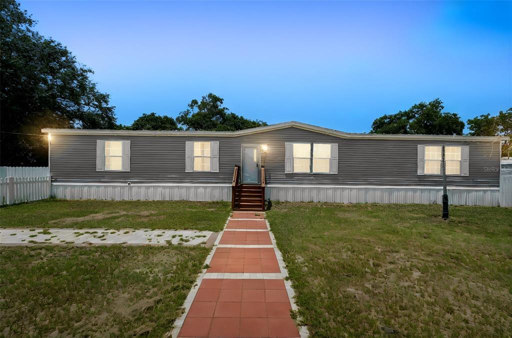 A gray manufactured home sits behind a white picket fence with a paved driveway — 618 1 ST STREET, POLK CITY, FL