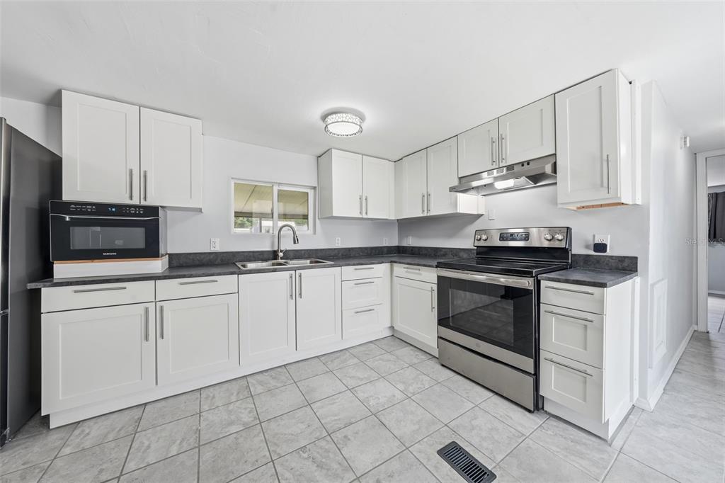 A kitchen with white cabinets, stainless steel appliances, dark countertops, and light gray tile flooring — 44945 2ND STREET, DELAND, FL