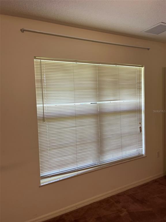 An empty bedroom features brown wall-to-wall carpeting, beige walls, and a window with horizontal blinds — 8451 SW 14TH LANE, OKEECHOBEE, FL