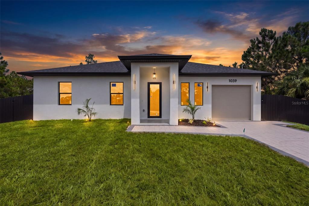 A modern single-story house with a gray exterior, a central entryway, and a paved driveway — 1039 BASSINGER AVENUE S, LEHIGH ACRES, FL