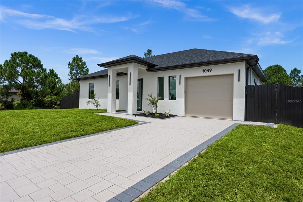 A modern single-story house features a white stucco exterior, a paved driveway, and a garage — 1039 BASSINGER AVENUE S, LEHIGH ACRES, FL