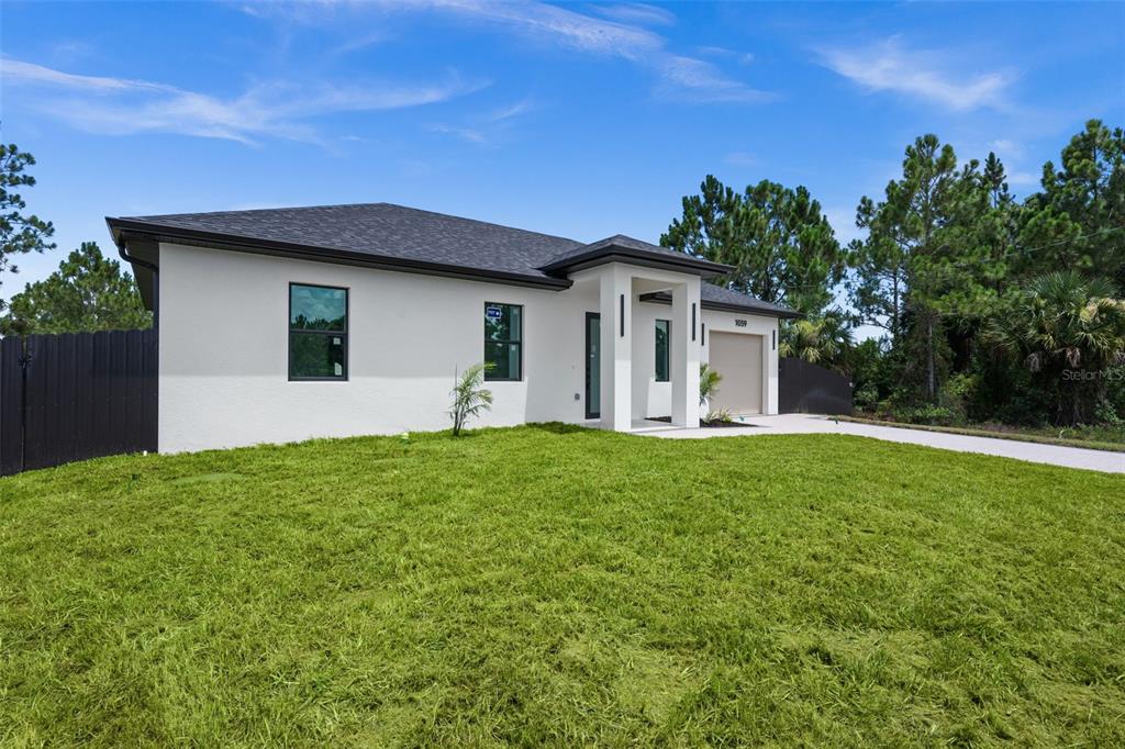 A modern, white single-story house with a dark roof and a concrete driveway — 1039 BASSINGER AVENUE S, LEHIGH ACRES, FL