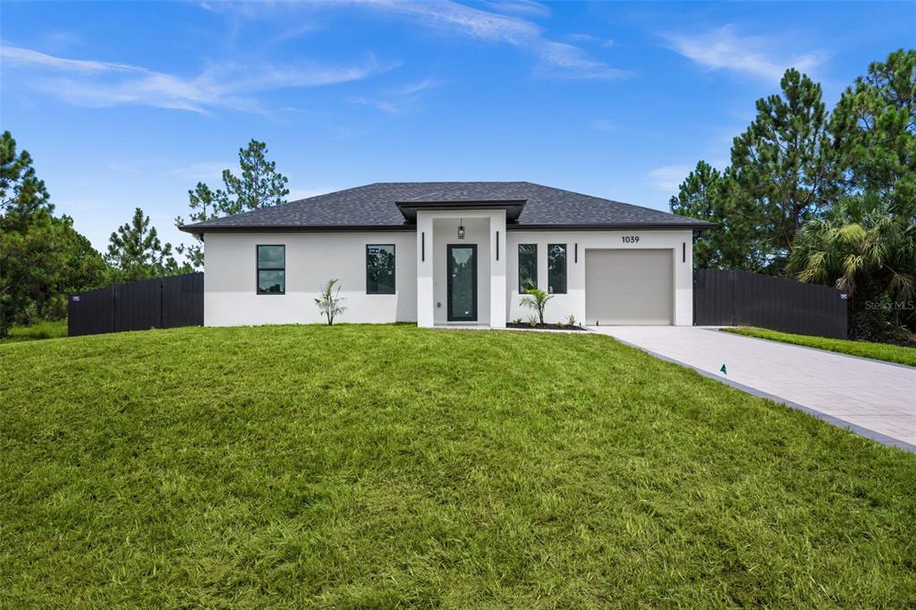 A single-story house with a white exterior, dark roof, and a paved driveway — 1039 BASSINGER AVENUE S, LEHIGH ACRES, FL