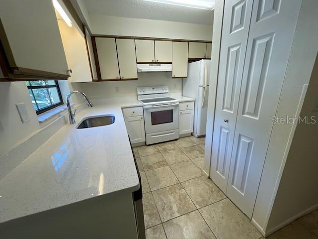 A kitchen features white cabinets, quartz countertops, a stainless steel sink, and white appliances — 2780 PARK DRIVE UNIT K-11, CLEARWATER, FL