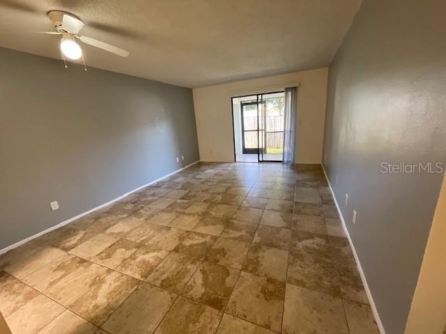 An empty room features light-colored tile flooring, gray walls, a ceiling fan, and sliding glass doors — 2780 PARK DRIVE UNIT K-11, CLEARWATER, FL