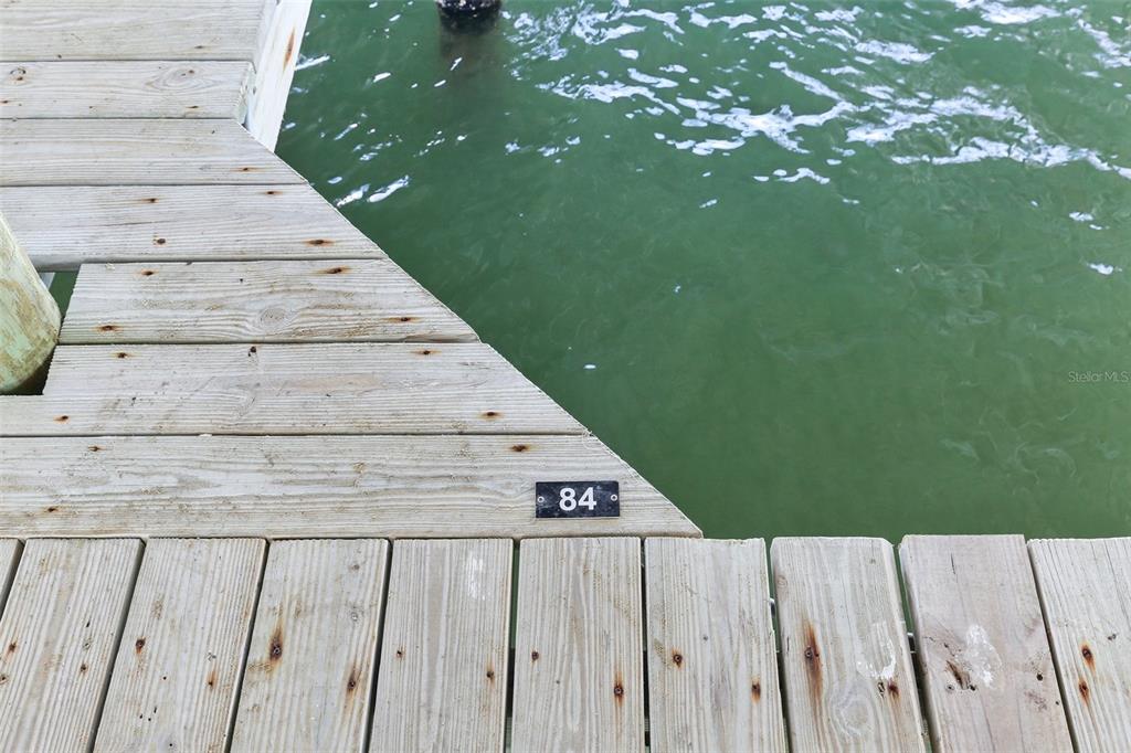 A wooden boat dock features a numbered identification tag on its edge above the water — 200 WINDWARD PASSAGE UNIT 84, CLEARWATER, FL