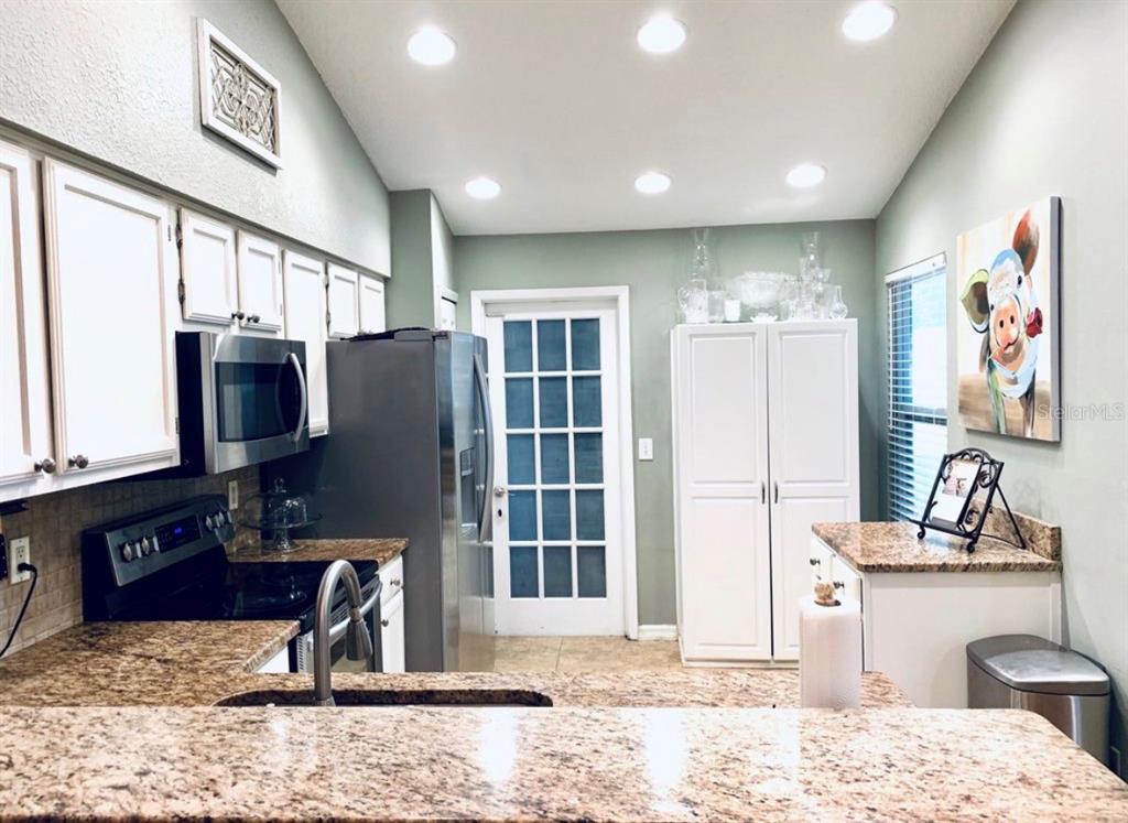 A kitchen features granite countertops, white cabinetry, stainless steel appliances, and a glass-paneled door — 7333 RADIANT CIRCLE, ORLANDO, FL
