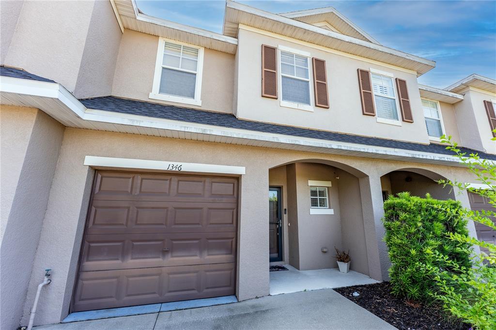 A two-story townhouse exterior features a brown garage door, beige stucco walls, and arched entryway — 1346 GRANTHAM DRIVE, SARASOTA, FL