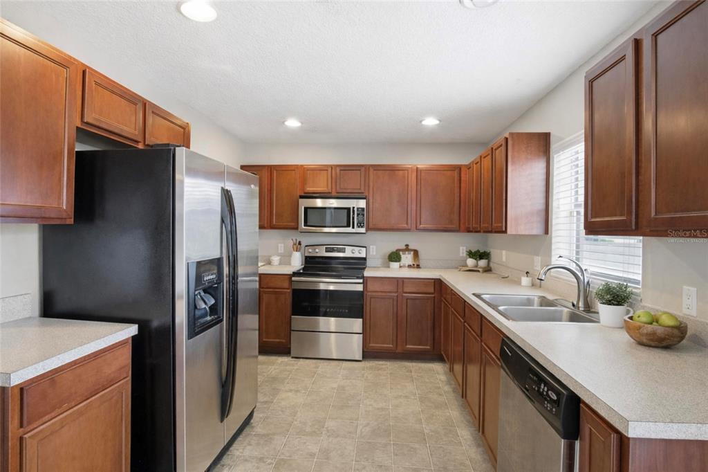 A kitchen features wood cabinets, stainless steel appliances, and light-colored countertops — 2463 MARTINS RUN, TAVARES, FL