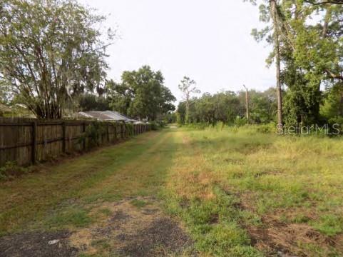 A grassy path runs alongside a wooden fence with trees and vegetation in the background — 5001 WHIPPOORWILL DRIVE, HOLIDAY, FL