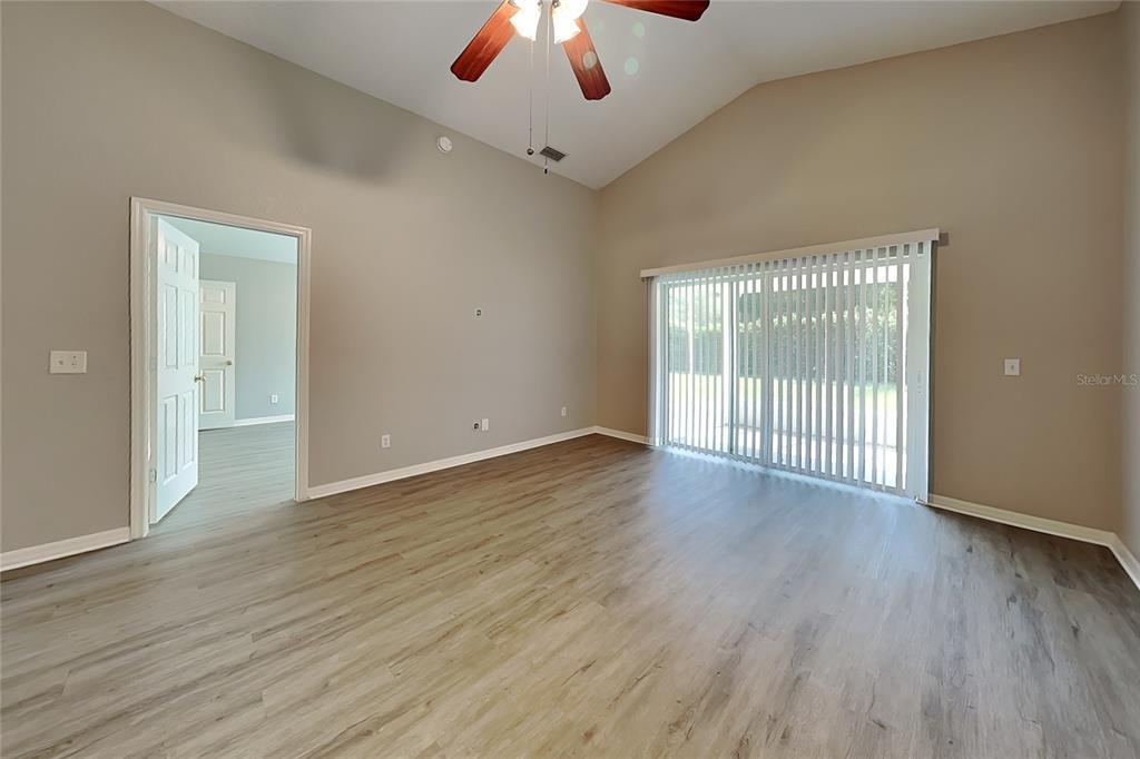 An empty room features light wood-look flooring, vaulted ceilings, a ceiling fan, and sliding doors — 3111 BUCKEYE POINTE DRIVE, WINTER HAVEN, FL