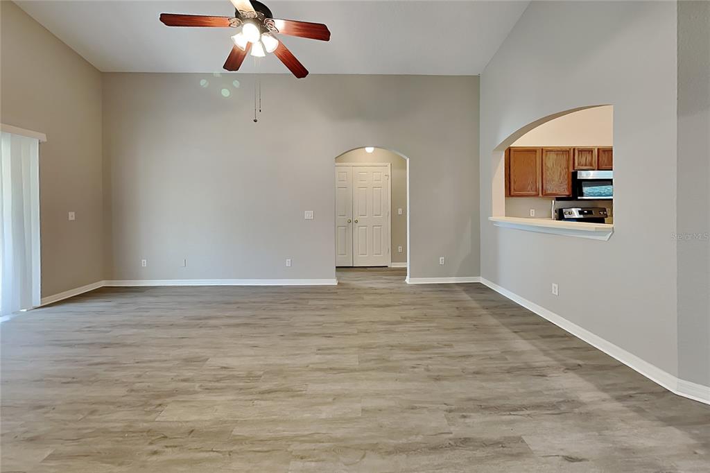 A spacious living room features light gray walls, wood-look flooring, and a kitchen pass-through window — 3111 BUCKEYE POINTE DRIVE, WINTER HAVEN, FL