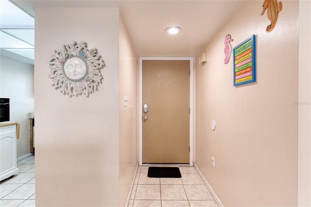 A tiled entryway features a tan door, a sun-themed wall hanging, and beach-themed decor — 1275 OCEAN SHORE BOULEVARD UNIT 2030, ORMOND BEACH, FL